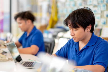 Asian garage worker or with blue uniform work in area of counter service with his co-worker and they look happy during working. Automotive part business and staff management system to support concept.の写真素材