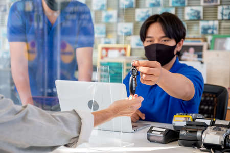 Remote car key that is sent by automotive shop worker to the customer who give hand to receive the key in the area of counter service during pandemic of Covid-19.の写真素材