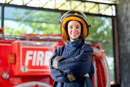 Firefighter with protective clothes stand with confidence action and smile in front of fire truck. She also smile with happy and love to work with this job.の写真素材