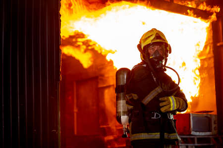 Fire on wall and ceiling in the kitchen behind firefighter man with protective and safety clothes stand with arm-crossed.の写真素材