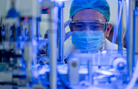 Close up face of factory worker touch protective eye glasses and look into part of machine with blue...