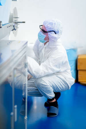Factory worker with full cover uniform sit and check or maintenance the mask producing machine in the factory workplace.の写真素材