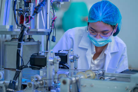 Factory worker woman with hygiene mask check part of machine in workplace area during mask producing...
