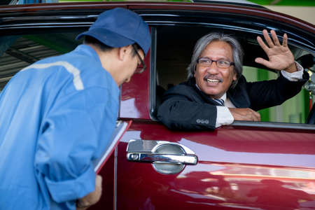 Automotive technician bow to senior customer sit in car and smile after finish fix the problem in...