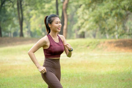 Close up Asian woman jogging in park or garden with green field and tree as background during morning time.の写真素材
