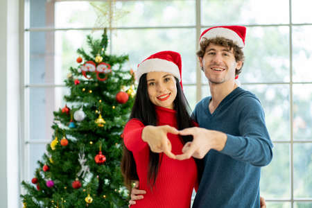 Couple young man and woman use hands to make symbol of heart and they stay in room with decoration of Christmas festival with happiness.の写真素材