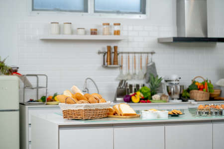 Basket of bread and set of cake and cookies on table inside the modern kitchen with other tools and accessories.の写真素材