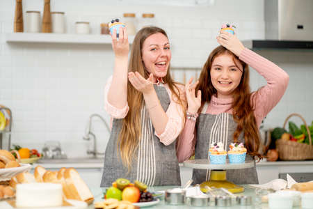 Caucasian mother and young daughter with apron hold cupcake and action of happy and funny during cooking in their home kitchen.の写真素材