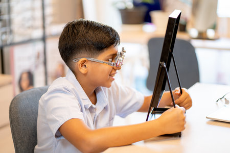 Indian boy has fun with wearing of special glasses for testing and look to mirror and smile in...