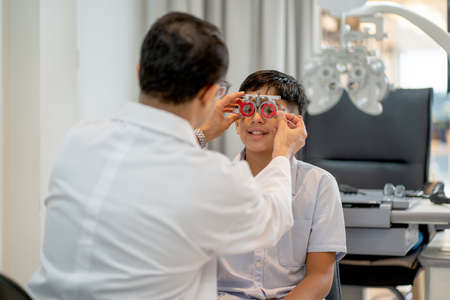 Optical staff or ophthalmologist adjust special glasses for testing eyesight of Indian boy in the shop.の写真素材