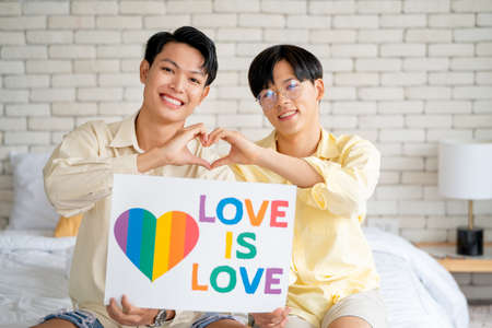 Couple gay or lgbt man sit on bed and hold banner to express their feeling and proud their relationship.の写真素材