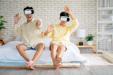 Couple Asian gay or lgbt man enjoy VR game together sitting on bed in bedroom. Concept of good activity and entertain for happiness.の写真素材