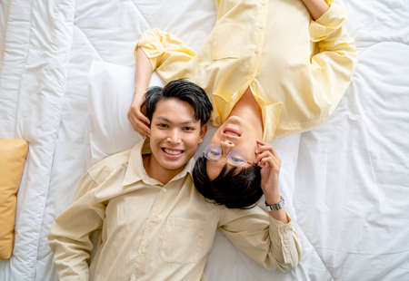 Top view of couple Asian gay or lgbt man lie on bed and set head close togther and they look happy also look at camera.の写真素材