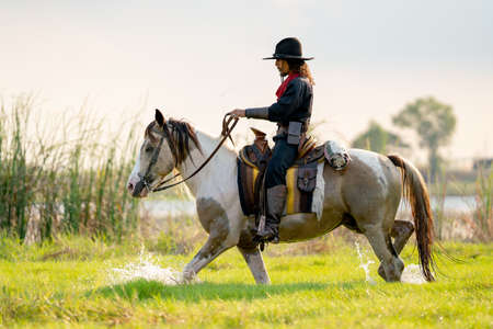 One cowboy with hat control horse to walk through grass field cover by water near river and show...