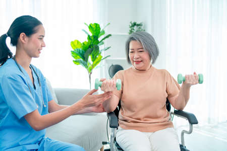 Asian nurse or doctor who work as homecare support staff help senior woman exercise with using...