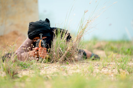 Terrorist with veil lie on the ground and point gun to the enemy in grass field with day light.