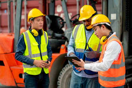 African American cargo container worker discuss with Asian technician using tablet in workplace area and they stay near forklift car.の写真素材