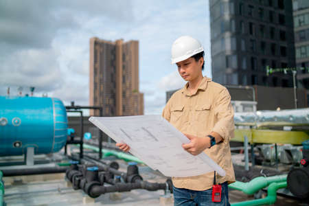 Asian engineer with white safety helmet hold and look the blue print paper of construction site also stay on terrace or deck of the building.の写真素材