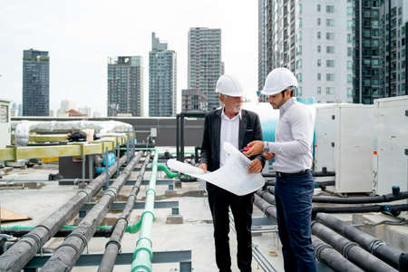 Wide shot of two engineers or technician man discuss together using building plan or drawing and...