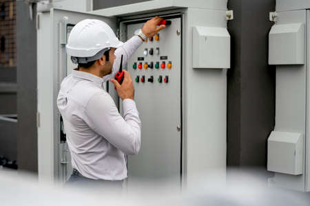 Caucasian engineer man or technician using walkie talkie to contact his coworker and ask for support about electrical control panel in construction site.の写真素材