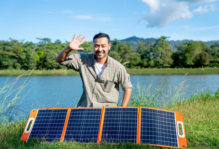 Asian man sit behide solar cells panel and wave hand with smiling to camera and he stay near the...