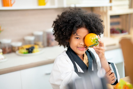 Lovely African American girl hold model of tomato and put on her eyes to make fun and look at camera during study in cooking class in the kitchen.の写真素材