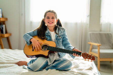 Lovely Caucacian girl enjoy to play guitar and sit on bed with day light in background and she look...