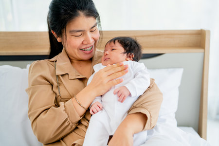 Close up Asian mother hold newborn baby and sit on bed in bedroom with day light and take care also...