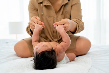Newborn baby hold hands of her mother after lie on bed and they look fun in bedroom with happiness.の写真素材