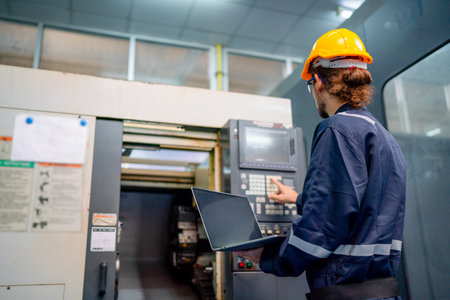 Lower view and Back of engineer or technician worker press button of big machine also hold laptop...