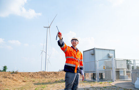 Engineer or technician worker point to left direction and stand in front of windmill or wind turbine in concept of work with green ecology support power.の写真素材