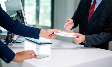 Close up hands of airline staff give boarding pass for flight to the customer at service counter in the airport.の写真素材