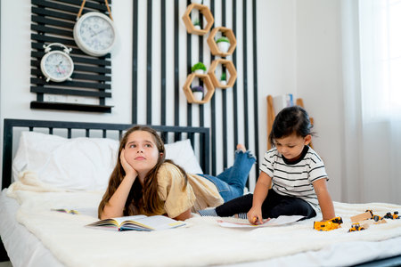Little Asian boy enjoy to play with toys on bed and stay near lovely girl lie on bed and action look like think about her homework in bedroom.の写真素材