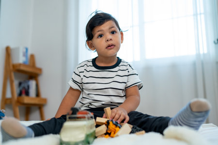 Portrait of little boy sit and enjoy to play serveral types of toys on floor of bedroom alone and also look at camera.の写真素材