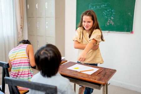 Caucasian girl stand in front of classroom and point to Asian boy look like angry with fun during learn in school.の写真素材