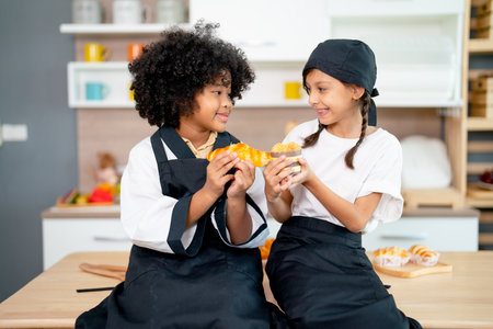 Two little girl sit on the table in kitchen and fun with use cupcake to play together during cooking...