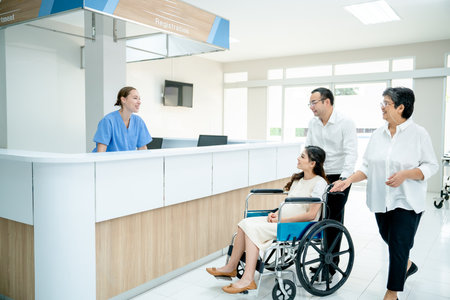 Asian family with grandmother, husband and pregnancy wife on wheelchair move pass area near reception or counter in hospital and greeting by Caucasian nurse.の写真素材