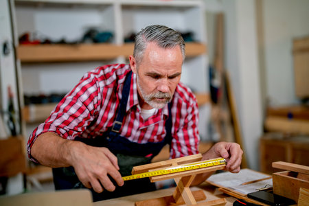 Professional senior carpenter man use tape measure to work with timber in woodwork factory workplace with happiness.の写真素材