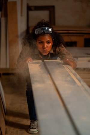 Carpenter woman blow debris and sawdust of wood product from timber in workplace.の写真素材