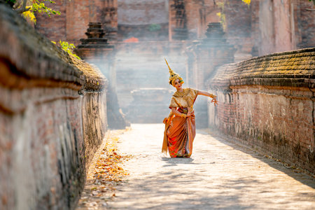 Asian beautiful woman with traditional dress dance with different actions on the way to ancient building and smoke or mist in the background with day light.の写真素材