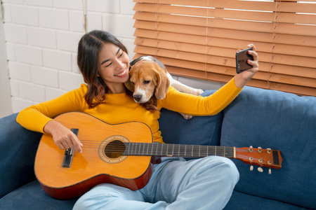 Young Asian girl enjoy to selfie with her dog during relax after play guitar on sofa in her house with day light.の写真素材