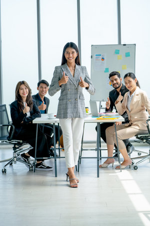 Asian pretty business woman stand in front of her co-workers sit in the back and she also show thumbs up and look at camera.の写真素材