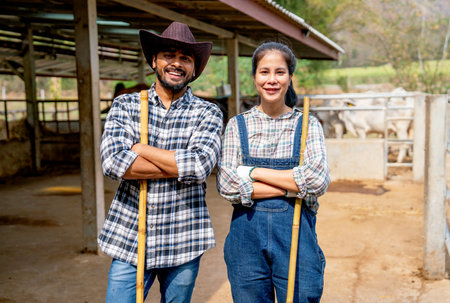 Portrait of Asian man and woman farmers carry broom and stand with arm crossed also look at camera with smiling in front of stable of cow look relax after clean the area.の写真素材