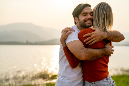 Close up Caucasian man hug with his lover woman near lake with romace and sunset light and they look happy and enjoy together.の写真素材
