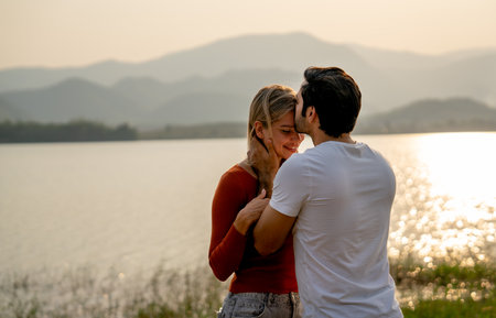 Back of Caucasian man kiss on forehead of beautiful woman with sunset light near lake and look romantic for couple love stay together.の写真素材