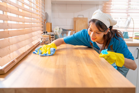 Asian housekeeper smile with happiness use towel to clean area in kitchen with day light and she...