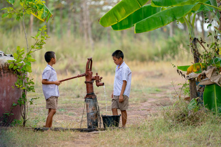 Two Asian boys use groundwater lever to get water for clean and also to grow some plants in the field.の写真素材