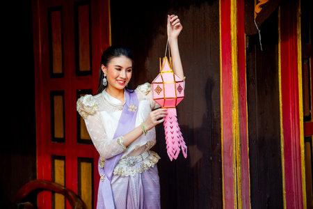 Young Asian woman with contemporary Thai dress stand and hold pink traditional lantern in area of ancient building and she look happy.の写真素材