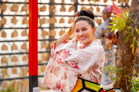 Portrait of pretty young woman wear japanese style dress and hold decoration on her hair also look at camera in front of row of lantern.の写真素材