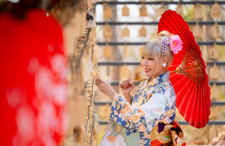 Portrait of pretty woman wear japanese style dress and hold red umbrella during attractive on wood banner in front of row of lantern.の写真素材
